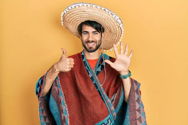 Молодой Латиноамериканец Держащий Мексиканскую Шляпу Показывающий Пальцами Номер Шесть Улыбаясь — стоковое фото