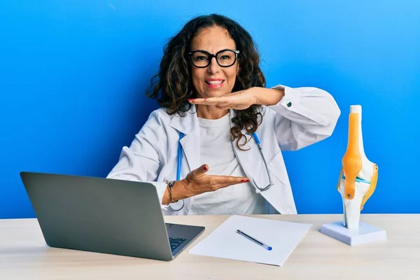 Beautiful middle age woman doctor at orthopedic clinic gesturing with hands showing big and large size sign, measure symbol. smiling looking at the camera. measuring concept.