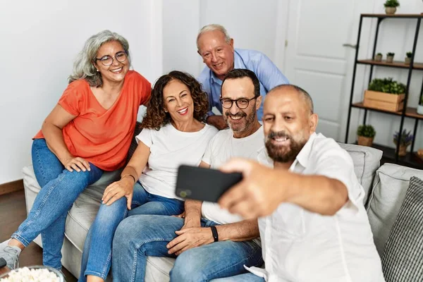 Gülümseyen bir grup orta yaşlı arkadaş evdeki akıllı telefonun yanında selfie çekiyorlar..
