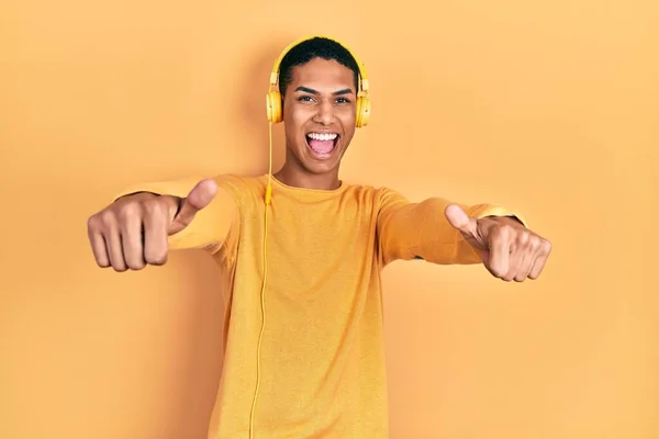 年轻的非洲裔美国人一边听着音乐 一边用耳机赞成用手做积极的手势 微笑着竖起大拇指 为成功感到高兴 优胜手势 — 图库照片