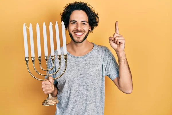 ハンサムなヒスパニック系の男を保持Menora Hanukka Jewishキャンドル笑顔でアイデアや質問を指差す指で幸せな顔 ナンバーワン — ストック写真