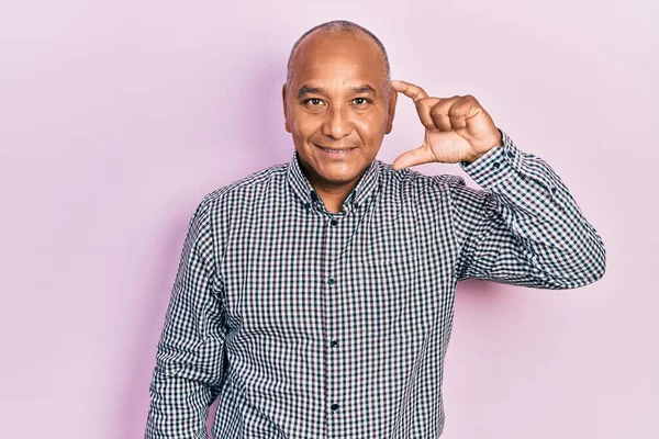 Orta yaşlı, sıradan kıyafetler giyen, gülümseyen, kendine güvenen, el hareketi yapan, parmaklarıyla işaret yapan ve kameraya bakan Latin bir adam. ölçüm kavramı. 