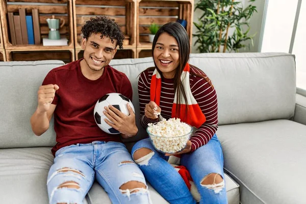 Evdeki kanepede oturan genç latin çift futbol maçını izliyor ve destekliyor..