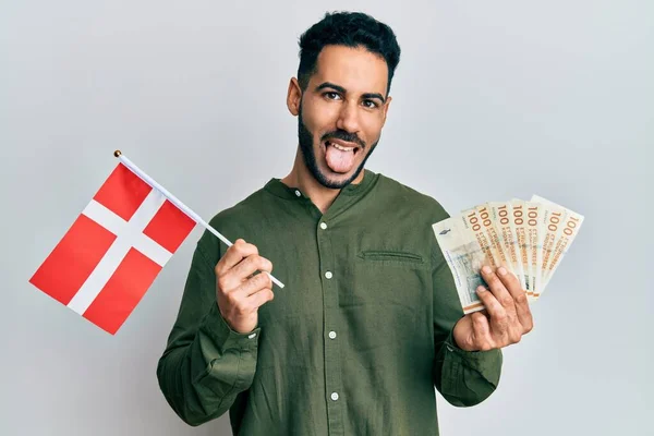 Młody Hiszpan Trzymający Flagę Denmarkową Banknoty Koronowe Wystające Języka Szczęśliwy — Zdjęcie stockowe