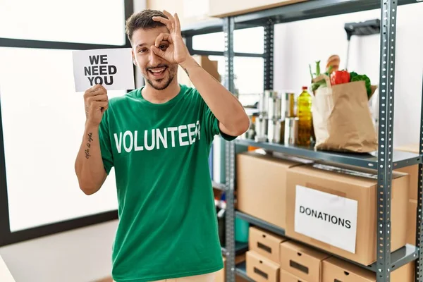 Joven Hombre Hispano Con Camiseta Voluntaria Sosteniendo Necesitamos Banner Sonriendo — Foto de Stock