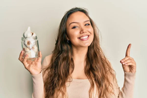 Genç İspanyol kız elinde bir bardak sarımsak tutarak gülümsüyor bir fikirle ya da soru işareti yaparak mutlu bir yüzle, bir numara 