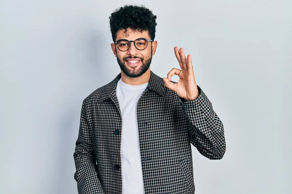 Sakallı, gözlüklü, gülümseyen genç bir Arap el ve parmaklarıyla 