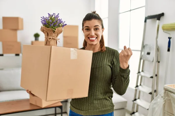 Genç İspanyol kadın hareket halindeyken karton kutu tutuyor. Gururla bağırıyor, zaferi kutluyor ve kollarını kaldırarak başarıyı kutluyor. 