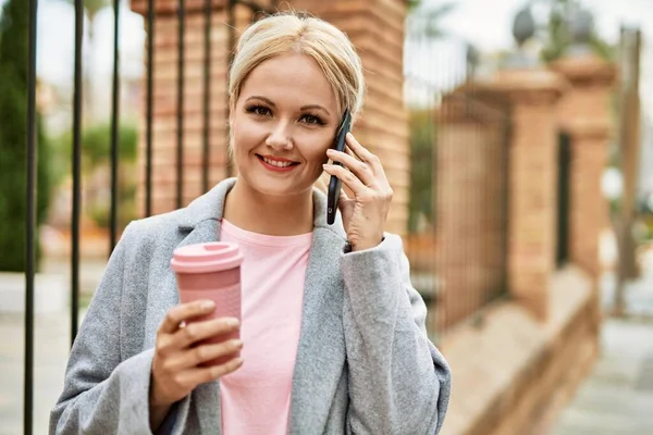 Sarışın iş kadını akıllı telefondan konuşuyor. Şehirde kahve içiyor..