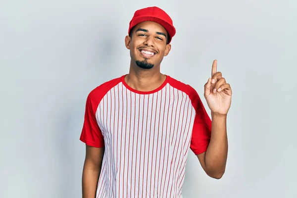 若いアフリカ系アメリカ人の男を着て野球の制服を着て笑顔幸せな顔を見て 親指を上げて側を指して — ストック写真