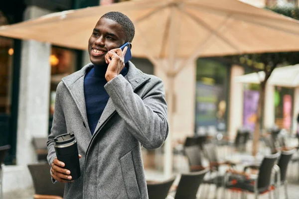 Genç Afrikalı Amerikalı adam akıllı telefonda konuşuyor. Şehirde kahve içiyor.