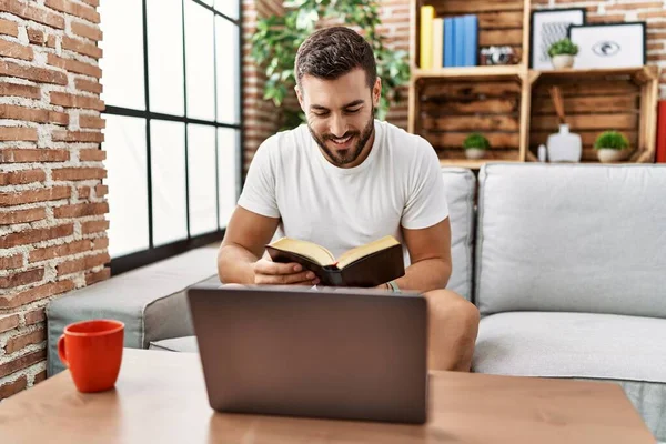 Genç İspanyol adam gülümsüyor evde kendinden emin bir şekilde kitap okuyor.