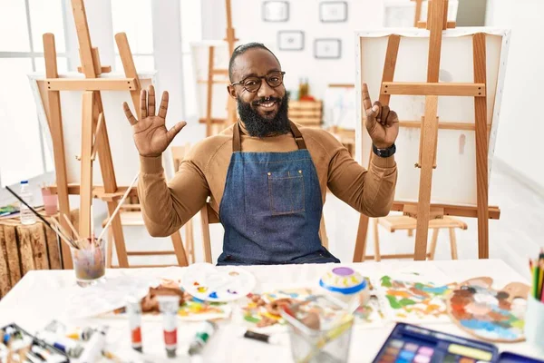 Sanat stüdyosundaki Afrikalı Amerikalı sanatçı kendini beğenmiş ve mutlu bir şekilde gülümserken altı numarayı gösterip işaret ediyor.. 