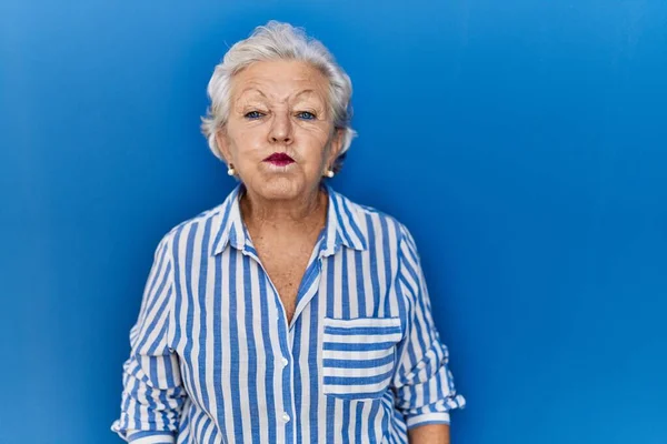 Mulher Sênior Com Cabelos Grisalhos Sobre Fundo Azul Soprando Bochechas — Fotografia de Stock