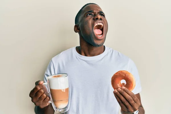 Νεαρός Αφροαμερικάνος Τρώει Ντόνατ Και Πίνει Καφέ Θυμωμένος Και Θυμωμένος — Φωτογραφία Αρχείου