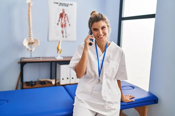 Mladá Blondýna Žena Uniformě Fyzioterapeuta Mluvit Smartphone Klinice — Stock fotografie
