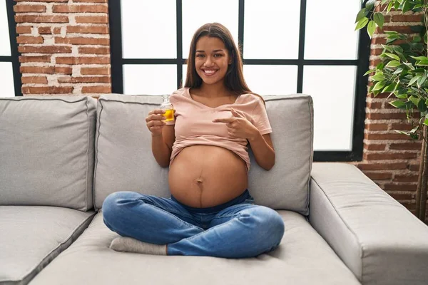 若いです妊娠中の女性保持モイスチャライザーオイルへ水和物腹笑顔幸せなポインティングとともに手と指 — ストック写真