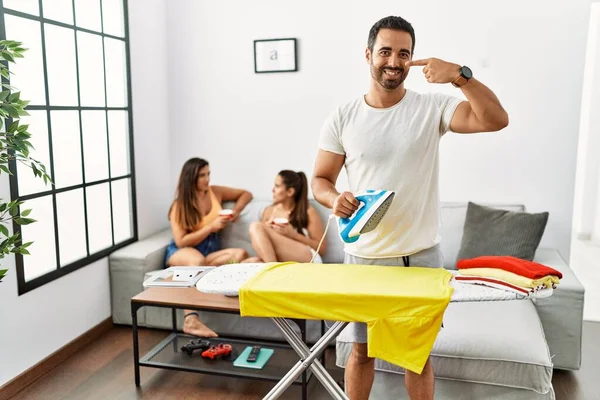 Elbiselerini ütüleyen genç İspanyol adam, elleri ve burunlarıyla işaret ediyor, neşeli bir şekilde gülümsüyor. güzellik konsepti 