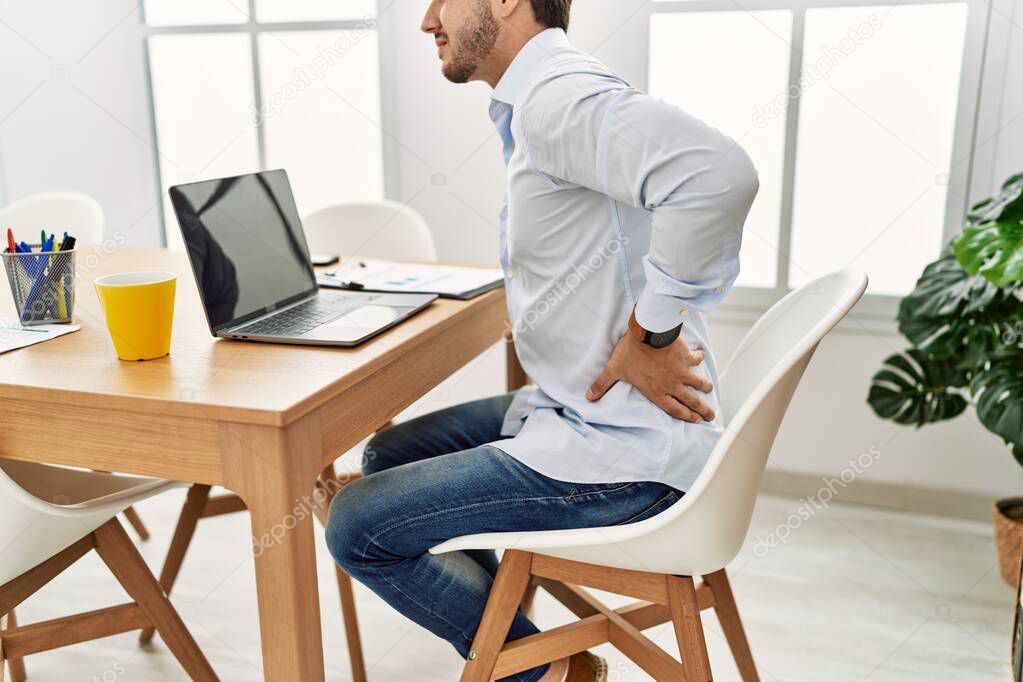 Young hispanic businessman working at the office. Sitting on the table with backache.