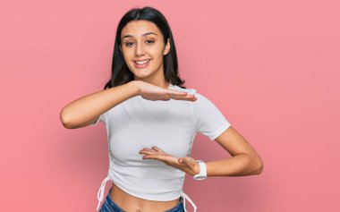 Latin kökenli genç bir kız, günlük beyaz tişörtler giyiyordu. Elleri büyük ve büyük bir işaret gösteriyordu. Ölçü sembolü. Kameraya bakıp gülümsüyor. ölçüm kavramı. 