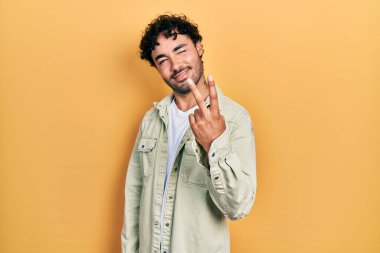 Gündelik kıyafetler giyen genç İspanyol adam iki numarayı gösterip işaret ederken kendinden emin ve mutlu bir şekilde gülümsüyor.. 