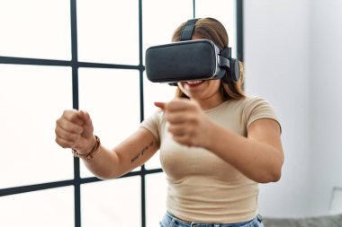 Genç İspanyol kadın evde sanal gerçeklik gözlüğü kullanarak video oyunu oynuyor.