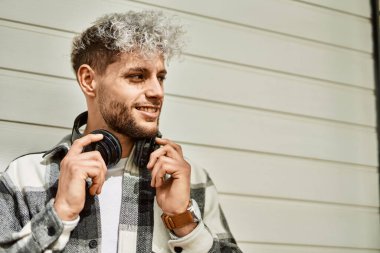 Şehirde kulaklık takarak mutlu gülümseyen genç İspanyol adam..