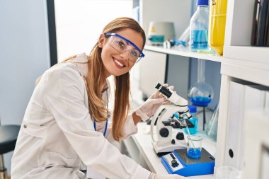 Laboratuvarda mikroskop kullanarak bilim adamı üniforması giyen genç sarışın kadın.