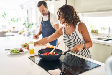 Orta yaşlı İspanyol çift mutfakta kendine güvenen yemekler pişiriyor.