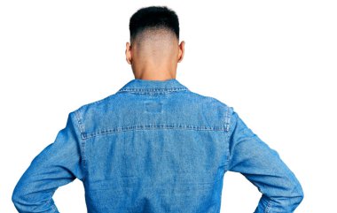 Sıradan kot ceket giyen, sakallı, genç, İspanyol bir adam kolları vücudunda geriye doğru bakıyor. 