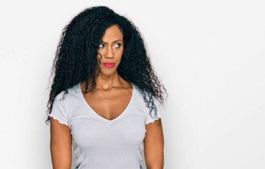 Orta yaşlı Afro-Amerikalı kadın, günlük beyaz tişört giyiyor. Gülümsüyor, yan tarafa bakıyor ve düşünüyor.. 