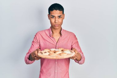 Genç Afro-Amerikan adam elinde kek tepsisi tutarken şüpheci ve gergin, sorun yüzünden somurtuyor. negatif kişi. 