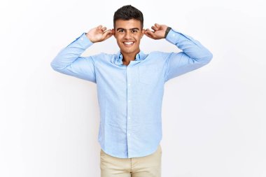İzole edilmiş arka planda duran İspanyol gömlekli genç adam parmaklarıyla kulaklarını çekerek gülüyor, komik bir jest yapıyor. deneme sorunu 