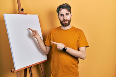 Ressam sehpasına işaret eden sakallı, beyaz bir adam bilgisiz ve kafası karışık bir ifade sergiliyor. şüphe kavramı. 