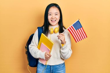 Genç Çinli değişim öğrencisi elinde Amerika bayrağı tutarken kahkahalarla gülüyor.. 