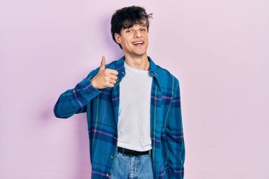 Yakışıklı hippi genç adam, günlük beyaz tişört ve klasik tişört giyip el hareketleriyle mutlu mesut selam veriyor. Kameraya bakıp başarıyı gösteren ifade. 