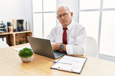 Ofiste çalışan kıdemli bir adam bilgisayar kullanıyor. Yüzünde ciddi bir ifadeyle rahatlamış. Basit ve doğal bir şekilde kameraya bakıyorsun.. 