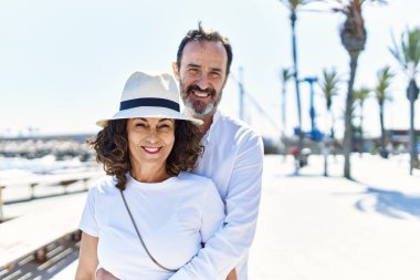 Orta yaşlı İspanyol çift, mutlu bir şekilde gülümsüyor ve gezinti alanında sarılıyorlar..