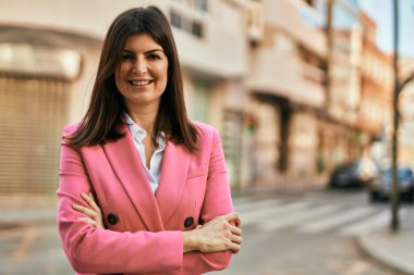 Güzel İspanyol iş kadını zarif bir ceket giyiyor. Şehre gülümsüyor, kolları kapalı.