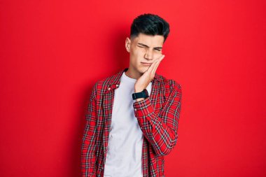 Günlük kıyafetler giyen genç İspanyol adam diş ağrısı ya da diş hastalığından dolayı acı dolu bir ifadeyle ağıza dokunuyor. dişçi 