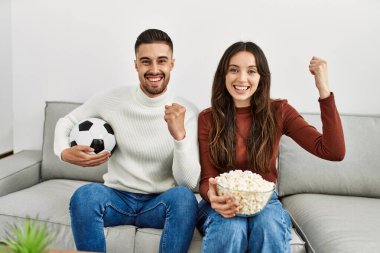 Genç İspanyol çift evde futbol maçı seyrediyor ve domuz eti yiyor..