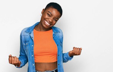 Genç Afro-Amerikalı kadın gündelik giysiler giyip çok mutlu ve heyecanlı bir şekilde kollarını kaldırıp, gülümseyerek ve başarı için bağırarak kazanan bir jest yapıyor. kutlama konsepti. 