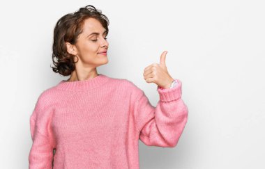 Genç İspanyol kadın günlük kıyafetler giyiyor. Gururlu görünüyor, gülümsüyor. Kenarda baş parmak hareketi yapıyor. 