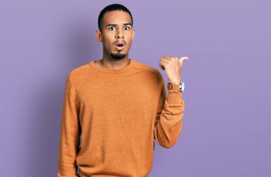 Gündelik giysiler giymiş genç Afro-Amerikan bir adam elleri yandan işaret ederek şaşırdı, ağzı açık hayret içinde kaldı.. 