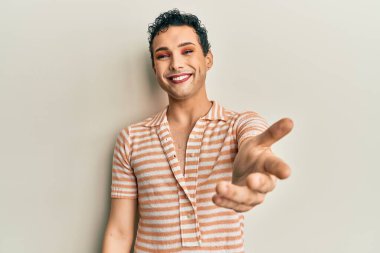 Makyaj yapan yakışıklı, sıradan bir tişört giyen, dostça gülümseyen, selamlaşmak için elini sıkan bir adam. başarılı iş. 