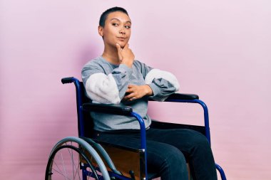 Kısa saçlı, eli çenesinde tekerlekli sandalyede oturmuş soru soran, düşünceli bir İspanyol kadın. Düşünceli bir yüzle gülümsüyor. şüphe kavramı. 