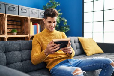 Evdeki kanepede oturan İspanyol görünümlü genç adam.