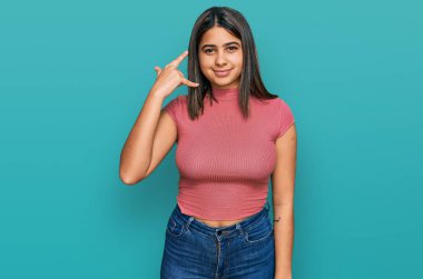 Sıradan tişörtler giyen, gülümseyen, el ve parmaklarıyla telefon hareketi yapan, telefonda konuşan İspanyol bir kız. iletişim kavramları. 