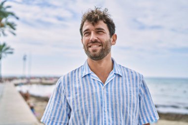 Genç İspanyol gülümseyen adam sahilde mutlu bir şekilde duruyor..