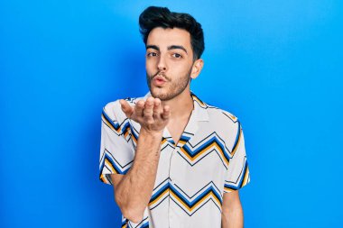 Gündelik giysiler giymiş genç İspanyol bir adam kameraya bakıp havada bir öpücük savuruyor ve sevimli ve seksi oluyor. aşk ifadesi. 